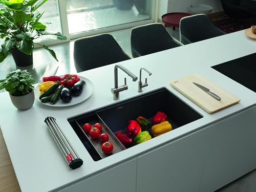 Black undermount granite kitchen sink installed in white countertop with red peppers and vegetables inside, chrome faucet vis