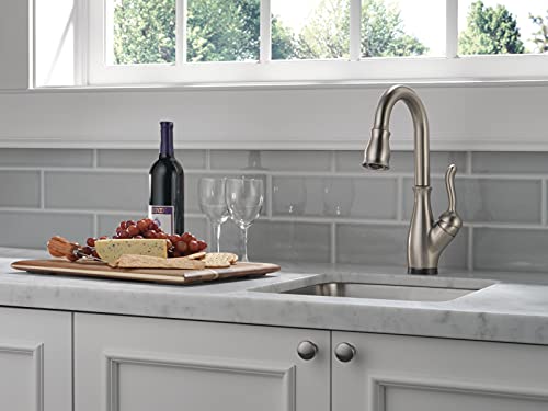 Stainless steel single-handle pull-down faucet with curved spout installed above kitchen sink next to food and wine.