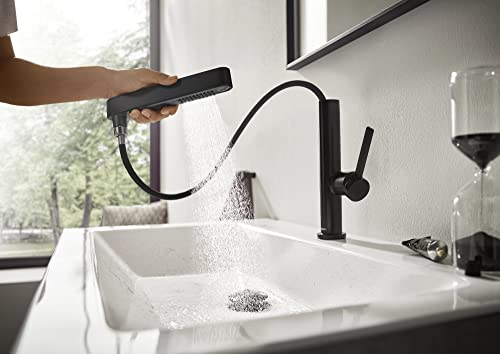 Matte black single-hole kitchen faucet with pull-out spray head extended over white sink, spraying water.