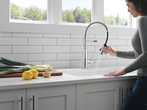Chrome single-handle pull-down kitchen faucet with coiled spray head over white sink in gray cabinetry.