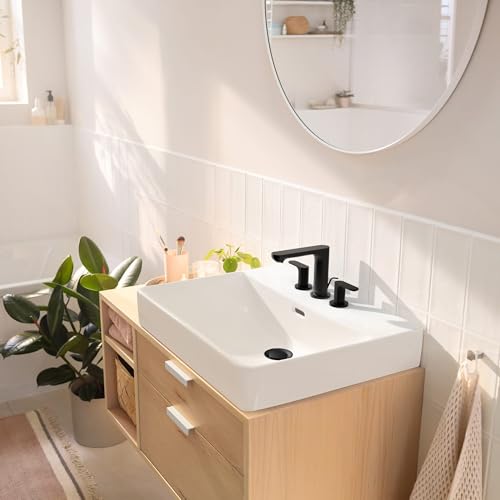 Matte black widespread bathroom faucet with two handles installed on white rectangular sink in modern bathroom vanity.
