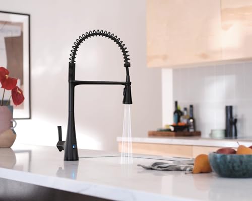Matte black high arc kitchen faucet with coiled spring neck and pulldown sprayer head installed on white countertop.