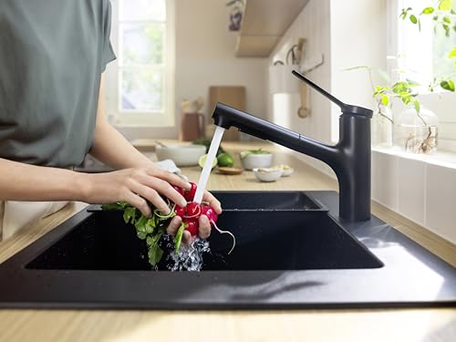 Matte black pull-out kitchen faucet with spray nozzle rinsing red radish over black sink.