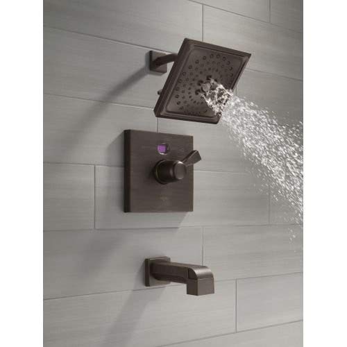 Venetian bronze shower valve trim kit with square showerhead and tub spout mounted on tile wall with water flowing.
