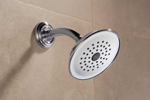 Chrome raincan shower head with perforated face mounted on curved arm against beige tile wall.