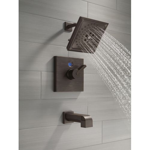 Polished brass shower arm mounted on tile wall with square showerhead and control valve.