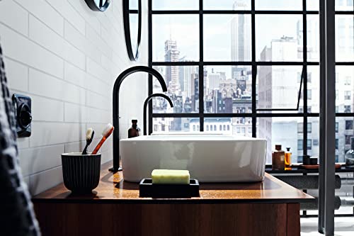 Matte black single-hole faucet with curved spout mounted on white vessel sink in modern bathroom with city skyline view.