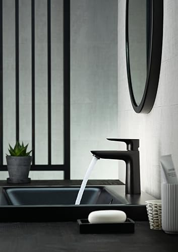 Matte black single-hole bathroom faucet with curved spout and pop-up drain, water running into black rectangular sink.