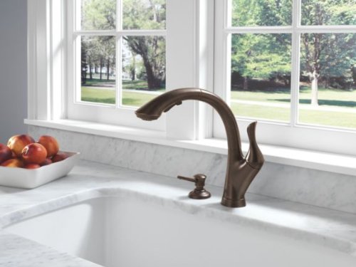Venetian bronze single-handle kitchen faucet with curved spout installed above white undermount sink.