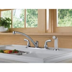 Chrome two-handle kitchen faucet with curved spout and separate spray nozzle on white sink.