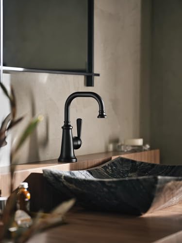 Matte black single-handle bathroom sink faucet with curved spout and traditional design mounted on wooden vanity.