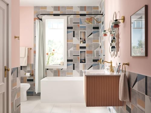 Brushed gold single-handle tub and shower trim kit mounted on bathroom wall above white bathtub with geometric tile surround.