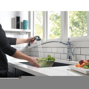 Champagne bronze single handle pull-out kitchen faucet with spray head extended over sink basin.