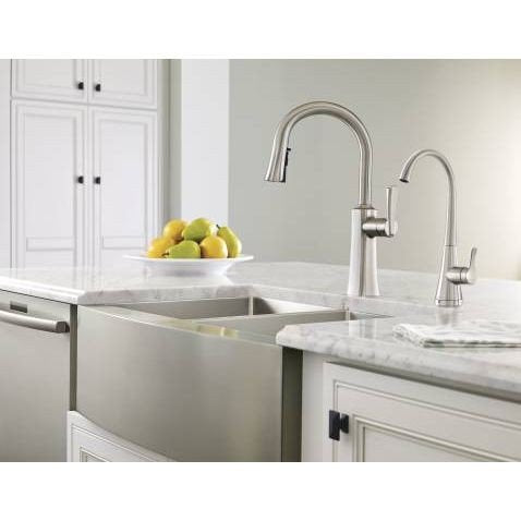 Chrome kitchen faucet with curved spout and spray head mounted on marble countertop next to farmhouse sink.