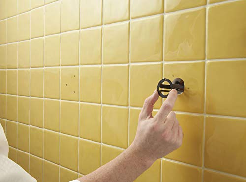 Hand installing chrome circular anchor fixture into yellow tile wall.