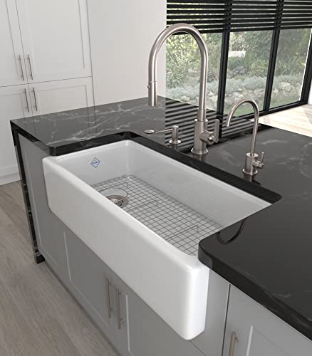 Satin nickel curved soap dispenser mounted on dark countertop next to kitchen sink faucet.
