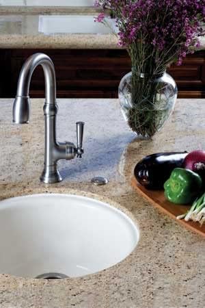 Satin bronze pull-down faucet with curved spout installed above undermount sink on granite countertop.