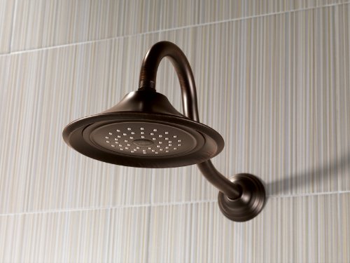 Venetian bronze shower head with curved arm and perforated round face mounted on tiled wall.