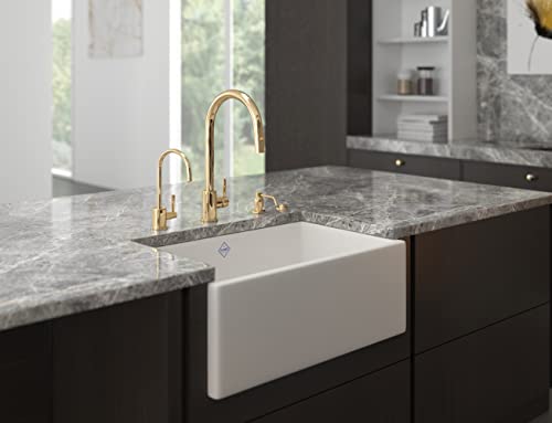 Satin English gold soap dispenser with curved spout mounted on gray marble countertop next to white farmhouse sink.