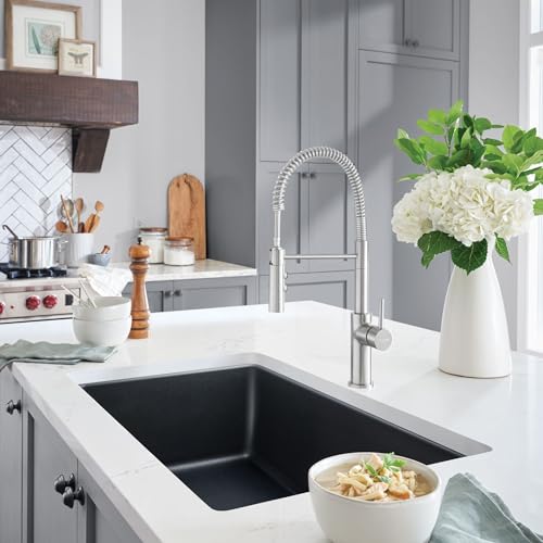 Anthracite single bowl sink mounted in white countertop with chrome pull-down faucet in modern kitchen.