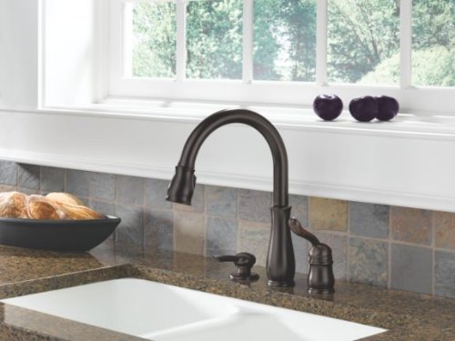 Venetian bronze soap and lotion dispenser pump mounted on kitchen sink countertop next to faucet.
