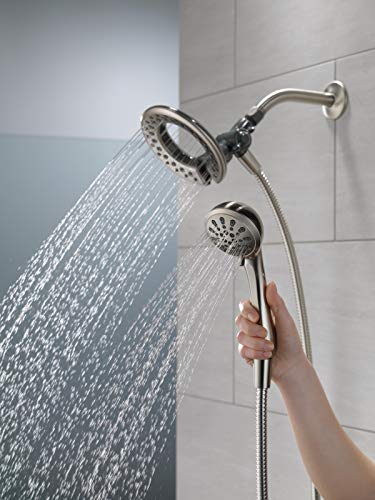Brushed nickel dual showerhead system with upper rainfall head spraying water and lower handheld head held in hand.