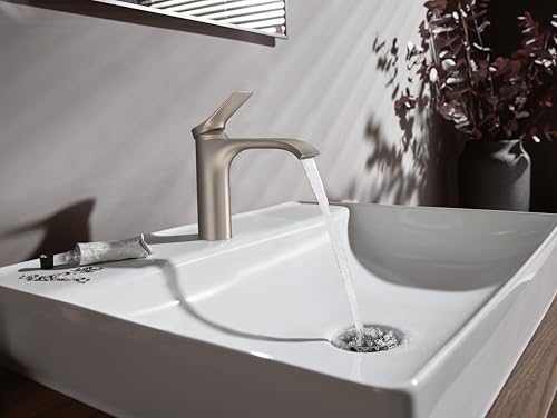 Brushed nickel single-hole faucet with arched spout installed on white sink with running water and pop-up drain.
