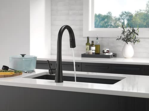 Black pull-down kitchen faucet with curved spout installed in white countertop sink.