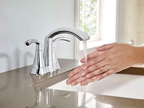 Chrome two-handle bathroom faucet with curved spout and water flowing over hand.