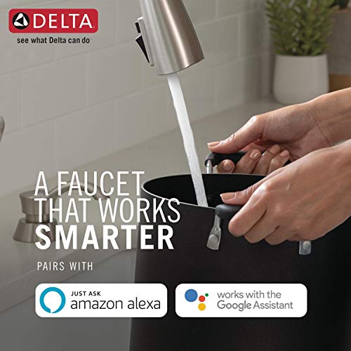 Stainless steel kitchen faucet with pull-down sprayer mounted over a black sink, hand activating water stream.