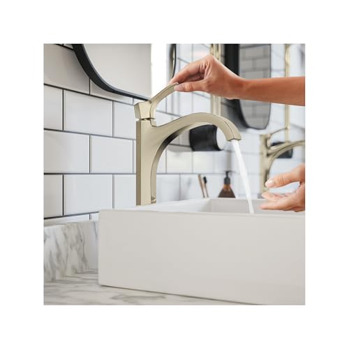 Polished nickel single-hole bathroom faucet with curved spout and hands demonstrating water flow over white sink.
