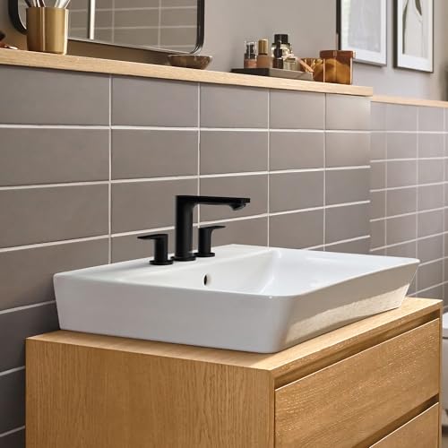 Matte black widespread bathroom faucet with two handles mounted on white vessel sink above wooden vanity.