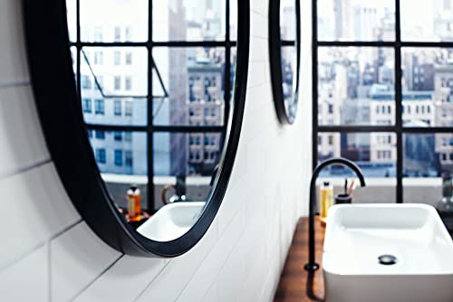 Matte black single-hole faucet with curved spout mounted on white bathroom sink counter next to round mirror.
