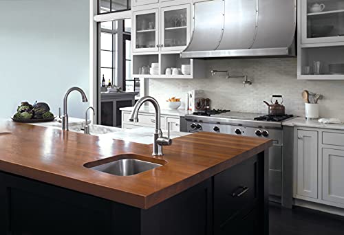 Steel optic wall-mounted pot filler faucet with curved spout installed above kitchen island sink.