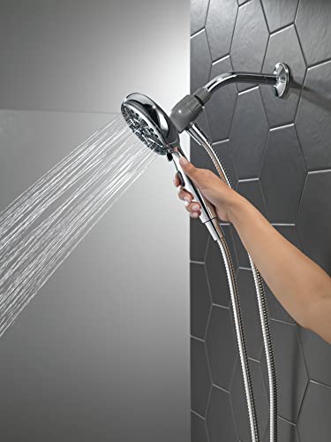 Chrome hand shower with magnetic dock mounted on subway tile wall, water spraying from showerhead held in hand.