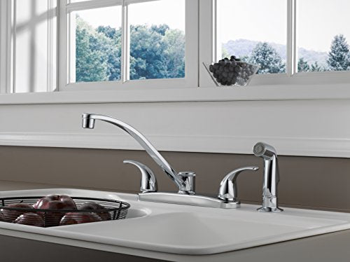 Chrome kitchen faucet with curved spout and two handles installed on white countertop with sprayer attachment.