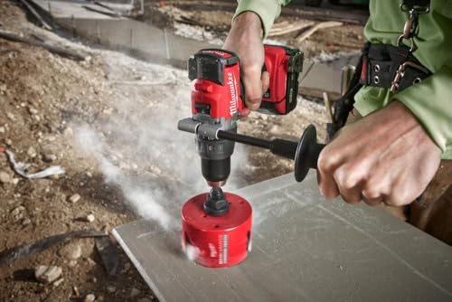 Red hole saw with carbide teeth attached to power drill, positioned on metal surface outdoors.