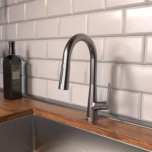 Brushed black chrome pull-down kitchen faucet with curved spout mounted above sink with white subway tile backsplash.
