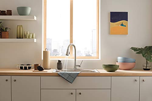 Stainless steel single-handle pull-down kitchen faucet with curved spout installed above white sink in gray cabinet.
