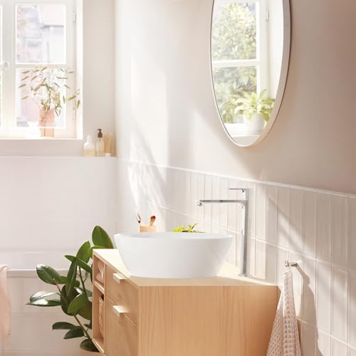 Chrome single-hole bathroom faucet with tall angular spout mounted on white vessel sink in wooden vanity.