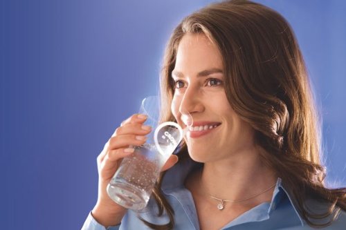 Woman holding a clear glass filled with water against a blue background.
