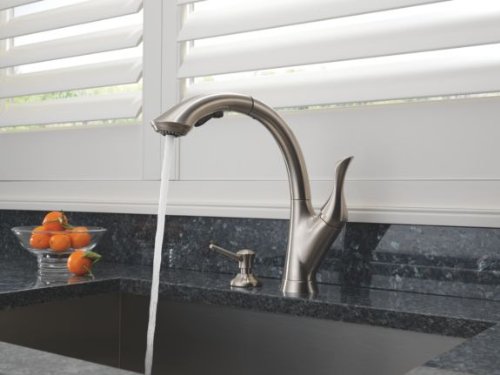 Stainless steel soap and lotion dispenser with curved spout mounted on dark countertop near sink.