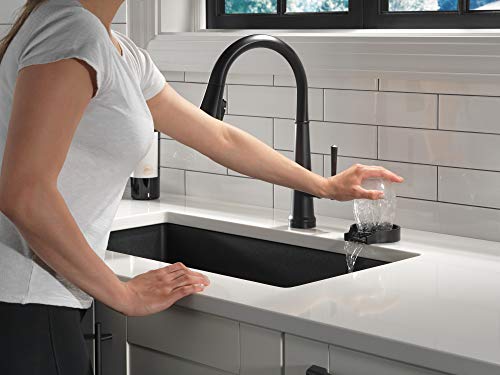 Black metal faucet with pull-down sprayer rinsing a glass over kitchen sink.