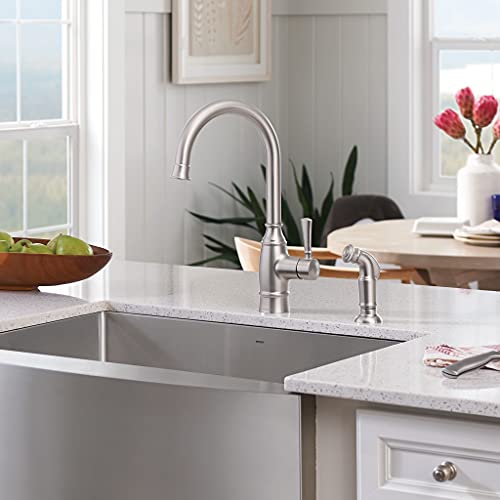 Stainless steel undermount farmhouse sink with apron front and single bowl, installed in white kitchen countertop.