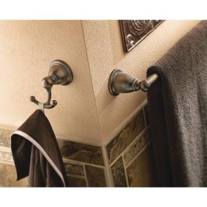 Moen double robe hook in brushed nickel mounted on beige bathroom wall with towels hanging from hooks.