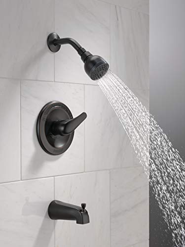 Oil rubbed bronze tub and shower trim with single-handle valve, spout, and overhead showerhead mounted on white tile wall.
