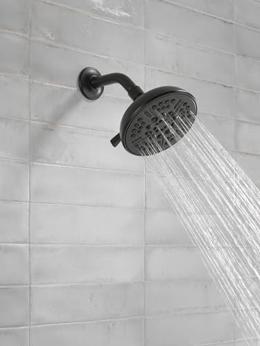 Matte black round shower head with curved arm mounted on white subway tile wall, water streaming downward.