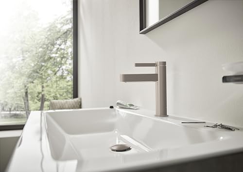 Brushed nickel single-hole faucet with cylindrical spout installed on white bathroom sink with pop-up drain.