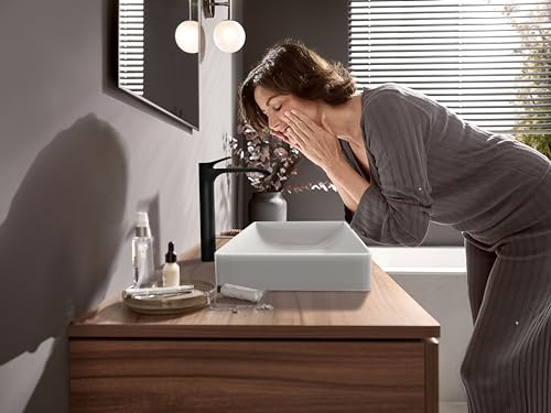 Matte black single-hole bathroom faucet installed above white vessel sink on wooden vanity.