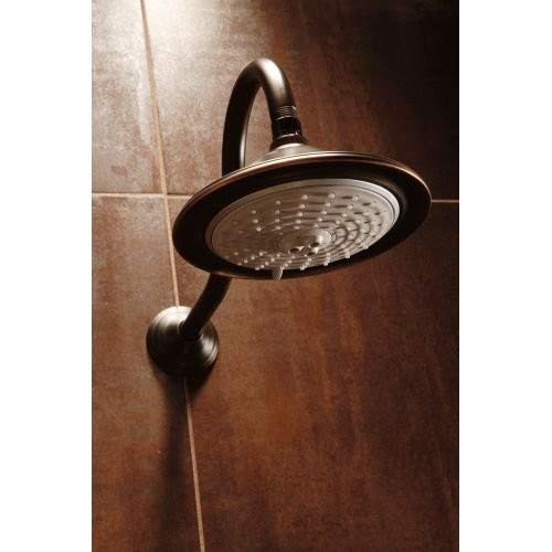 Stainless steel shower head with curved arm and circular spray face mounted on tiled bathroom wall.